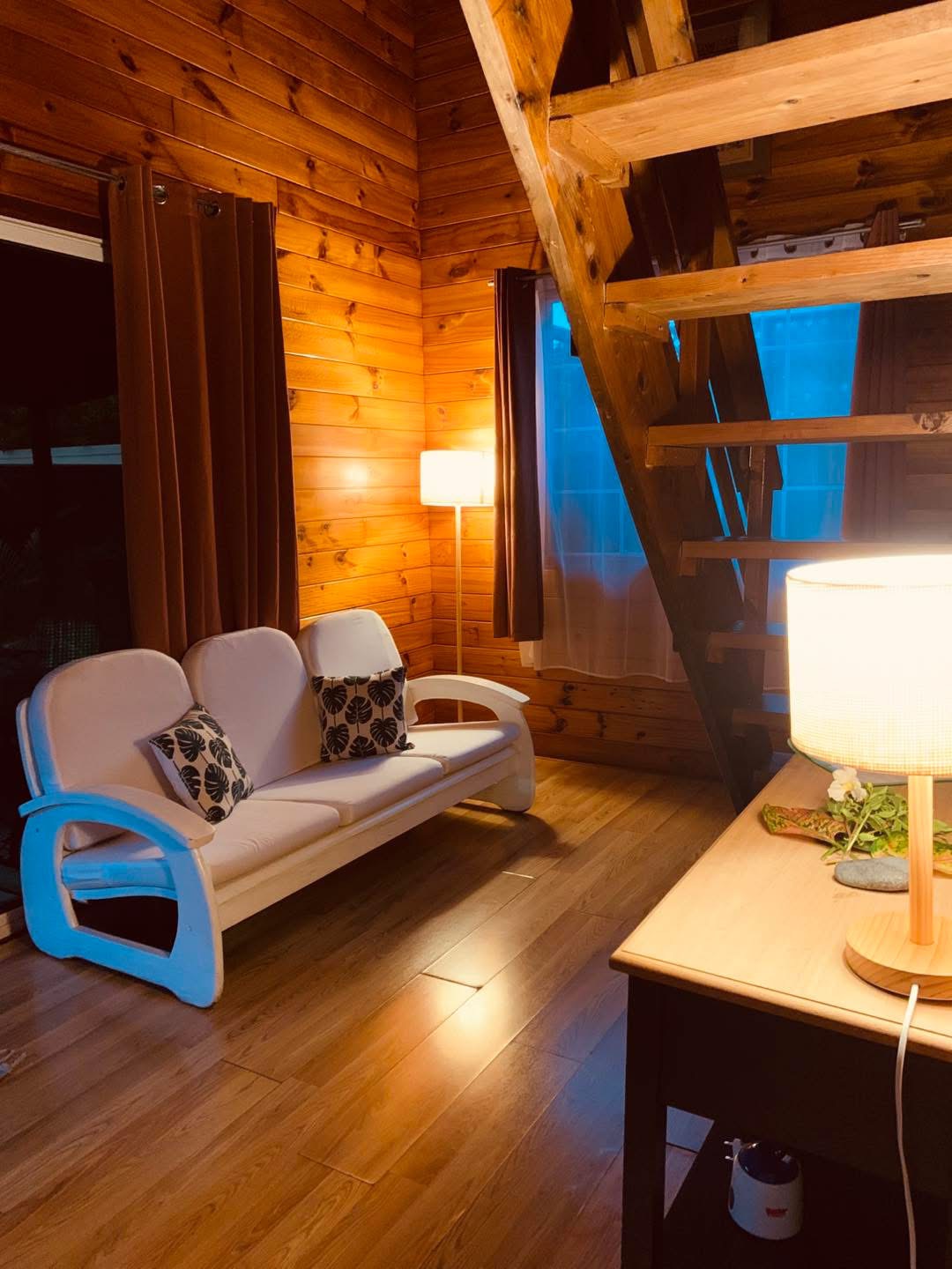 Salon chaleureux en bois avec canapé blanc, lampes et escalier vers la mezzanine
